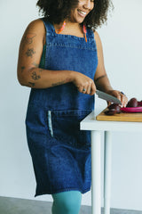 May include: A person wearing a blue denim apron with a pocket and the words 'home is where the heart is' tattooed on their arm, chopping red beets on a wooden cutting board.