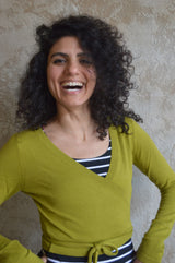 May include: A person wearing a green wrap sweater over a black and white striped shirt.