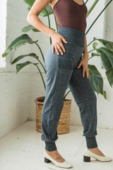May include: Dark gray jogger pants with a cuffed hem and a small pocket on the left thigh. The pants have a smocked waistband.