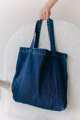 May include: A dark blue denim tote bag with two long straps. The bag is hanging from a white chair.